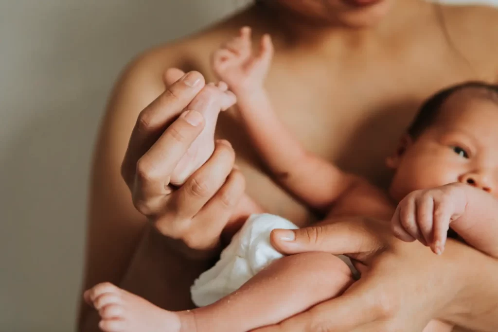 Recuperação pós-parto: mãe segurando bebê recém-nascido, representando o vínculo e os cuidados essenciais durante o pós-parto.